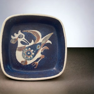 May include: A square ceramic dish with a blue glaze and a white rooster design. The rooster is stylized and has brown and blue accents.