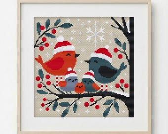 Op de afbeelding: Kruissteekkunstwerk van een vogelfamilie met kerstmutsen, zittend op een tak met rode bessen. De vogels zijn in tinten rood, blauw en oranje, tegen een beige achtergrond met een sneeuwvlokontwerp. Ingelijst in een licht houten frame.