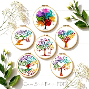 Könnte beinhalten: Sechs runde Stickrahmen aus Holz mit Kreuzstichmustern von Bäumen mit bunten Blättern im Aquarellstil. Die Motive zeigen verschiedene Baumformen, Herzmotive und eine Schaukel. Der Text Cross Stitch Pattern PDF ist deutlich zu sehen.