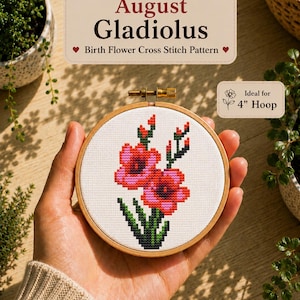 May include: A cross stitch pattern featuring a red and pink gladiolus flower with green stems and leaves, displayed in a wooden embroidery hoop. The text reads August Gladiolus Birth Flower Cross Stitch Pattern and Ideal for 4" Hoop.
