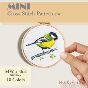 A cross stitch pattern of a yellow bird with black and blue markings perched on a branch. Mini cross stitch pattern.