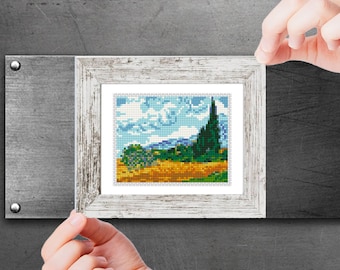 May include: A framed cross-stitch artwork depicting a landscape with a green tree, a field of yellow flowers, and a blue sky with white clouds.