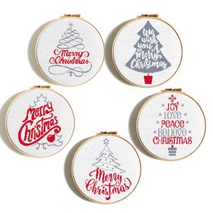 May include: Five round embroidery hoops with Christmas-themed cross-stitch designs. Each hoop features a white fabric with a different festive message in red and gray, including "Merry Christmas" and "Joy, Love, Peace, Believe Christmas."