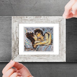 以下が含まれることがあります： 抱き合うカップルを描いた、額装されたクロスステッチのアートワーク。アートワークは、白い背景に茶色、黄色、青色の糸を使用しています。フレームは、白のアンティーク調です。