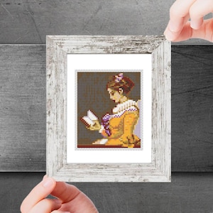 Puede incluir: Un bordado de punto de cruz enmarcado que representa a una mujer con un vestido amarillo leyendo un libro. La mujer tiene el pelo castaño y lleva una flor morada en el pelo.