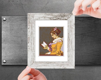 Op de afbeelding: Een ingelijst borduurwerk met kruissteek, waarop een vrouw in een gele jurk te zien is die een boek leest. De vrouw heeft bruin haar en draagt een paarse bloem in haar haar.