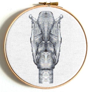 May include: A cross-stitch embroidery of a human larynx, displayed in a wooden hoop. The anatomical structure is rendered in shades of gray and white, creating a detailed and artistic representation of the vocal cords and surrounding cartilage.