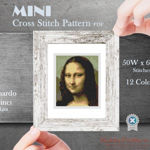 May include: A framed cross-stitch pattern of the Mona Lisa by Leonardo da Vinci. The pattern is labeled "MINI" and includes details: 50W x 60H stitches, 12 colors. The frame is white with a distressed finish.