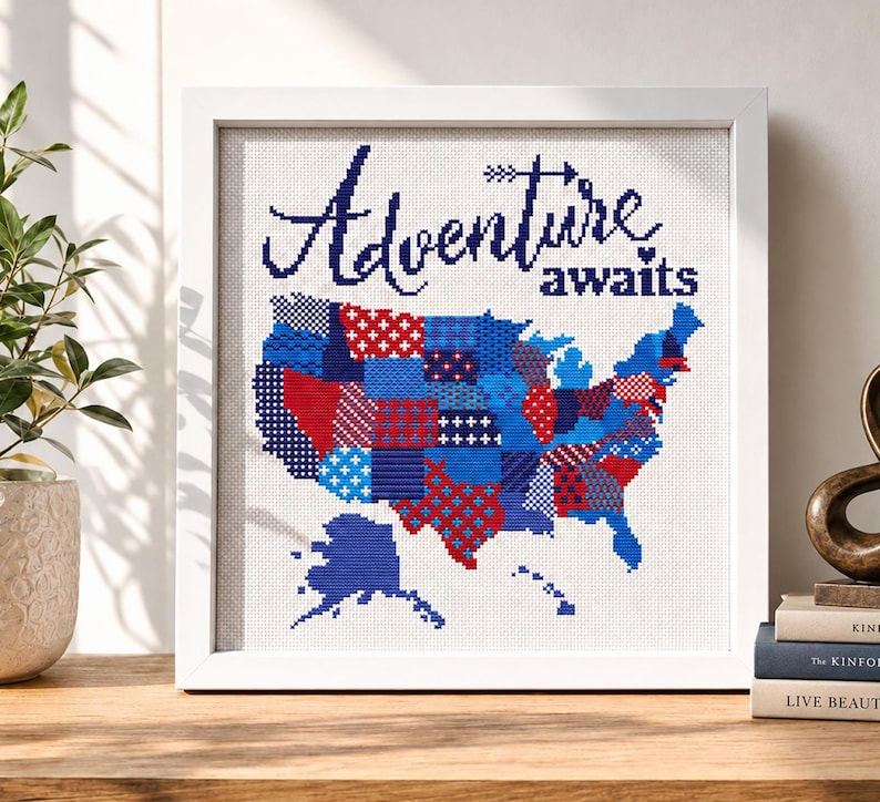Puede incluir: Una obra de arte en punto de cruz enmarcada con un mapa de los Estados Unidos. El mapa est&aacute; compuesto por patrones de patchwork rojos, blancos y azules. Las palabras "Adventure awaits" est&aacute;n bordadas en azul marino sobre el mapa.