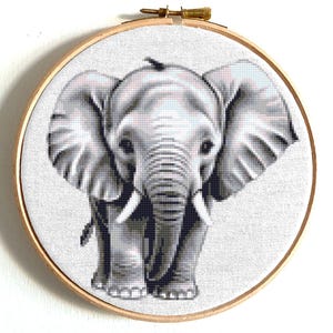 May include: A black and white cross-stitch embroidery of an elephant with a detailed face and large ears. The elephant is framed in a wooden hoop.