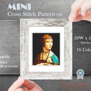 May include: A framed cross-stitch pattern of Leonardo da Vinci's "Lady with an Ermine." The image is a pixelated rendition of the painting, with a woman in a brown dress and a turquoise sleeve. The frame is white, and the pattern is 50 stitches wide and 59 stitches high.