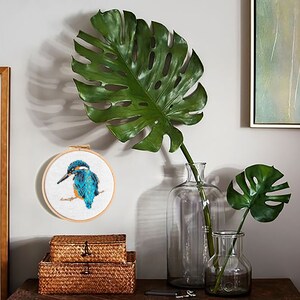 A blue and orange bird cross stitch pattern in a wooden hoop, hanging on a white wall.