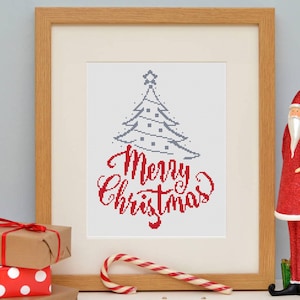 May include: A framed cross-stitch artwork with a Christmas tree design and the words "Merry Christmas" in red. A red and white candy cane, wrapped gifts, and a Santa Claus figurine are also visible.