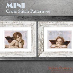 May include: Two framed cross stitch patterns of angels with wings. The angels are depicted with brown hair and are wearing white clothing. The frames are white with a distressed wood finish.