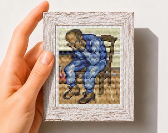 May include: A cross stitch pattern featuring a pixelated figure in blue clothing sitting on a chair with their head in their hands, framed in a white textured square frame. The text below reads Mini Art Cross Stitch Pattern PDF.