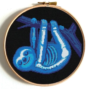 Könnte beinhalten: Kreuzstich-Stickerei mit einem blauen Faultier-Skelett, das an einem Ast vor schwarzem Hintergrund hängt. Das Kunstwerk ist in einem runden Holzreifen gerahmt und schafft eine einzigartige Wanddekoration.