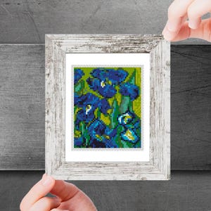 May include: A framed print of a painting featuring blue irises with green leaves and stems on a yellow background.
