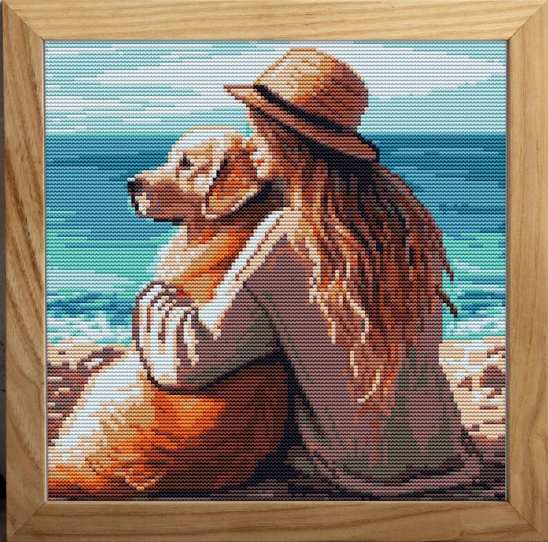 May include: Cross-stitch artwork in a wooden frame depicts a person with long brown hair and a straw hat embracing a golden retriever on a beach. The ocean and sky are in the background.