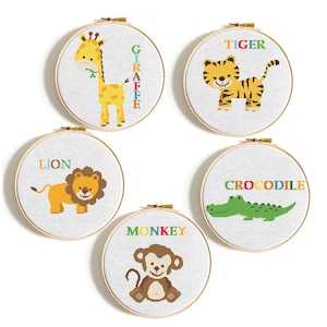 May include: Five circular embroidery hoops featuring animal designs. A giraffe, tiger, lion, monkey, and crocodile are shown in colourful cross-stitch. Each hoop has the animal's name in a matching colour.