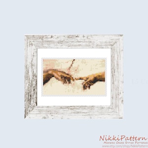 May include: A framed cross-stitch pattern featuring a portion of Michelangelo's "The Creation of Adam." The artwork depicts two hands nearly touching, rendered in a pixelated style. The frame is white with a distressed finish. The text "15 Colors" is visible.