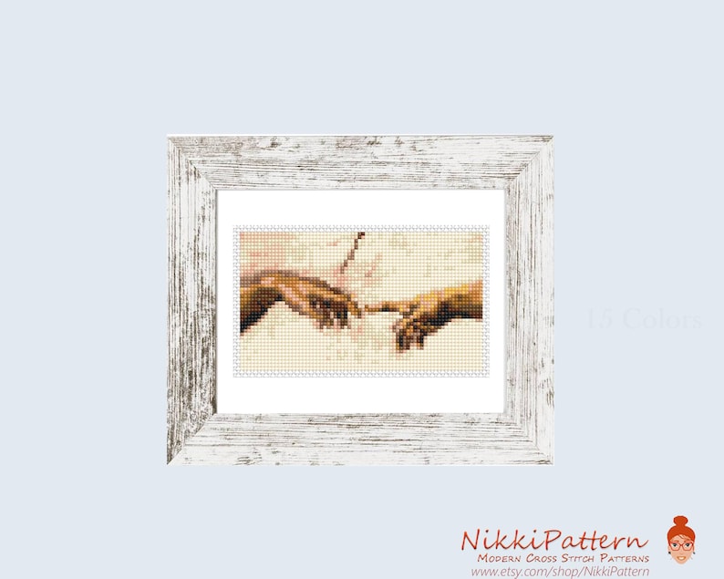 May include: A framed cross-stitch pattern featuring a portion of Michelangelo's "The Creation of Adam." The artwork depicts two hands nearly touching, rendered in a pixelated style. The frame is white with a distressed finish. The text "15 Colors" is visible.