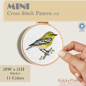 A cross stitch pattern of a yellow and green bird with black markings on a branch. The pattern is mini cross stitch pattern.