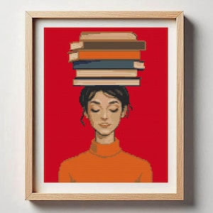 May include: A framed art print features a woman with closed eyes, balancing a stack of books on her head. The artwork is a cross-stitch style with a red background. The woman wears an orange turtleneck sweater.