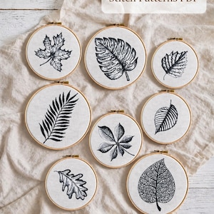 May include: A collection of eight cross-stitch patterns, each depicting a different leaf design in black and white, set within wooden embroidery hoops. The text reads "Set of 8 Cross Stitch Patterns PDF". Includes maple and fern leaves.