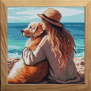 May include: Cross-stitch artwork in a wooden frame depicts a person with long brown hair and a straw hat embracing a golden retriever on a beach. The ocean and sky are in the background.