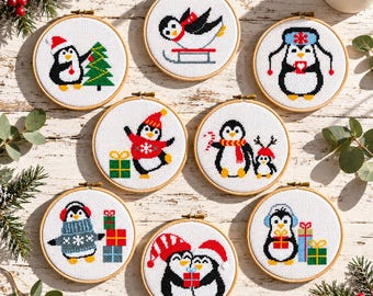 May include: Eight circular wooden embroidery hoops containing cross-stitch designs of penguins. The penguins are depicted in various winter scenes, including decorating a tree, sledding, wearing hats and scarves, and holding gifts on a white fabric background.