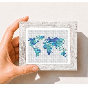 May include: A cross-stitch embroidery of a world map featuring shades of blue, teal, and green thread on a white fabric background. The artwork is encased in a rectangular, weathered white wooden frame with a textured, distressed finish.