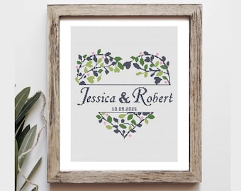 Può includere: Opera d'arte a punto croce in una cornice di legno. Il design presenta i nomi "Jessica & Robert" con la data "10.09.2025" sottostante. Foglie verdi e blu navy con accenti rosa formano bordi decorativi.
