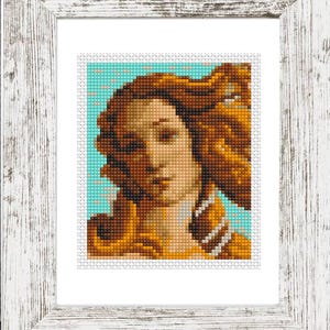 May include: Framed cross-stitch art featuring a portrait of a woman with long, flowing auburn hair. The artwork is set against a light blue background and framed in a distressed white wooden frame. The image is a close-up of the face.