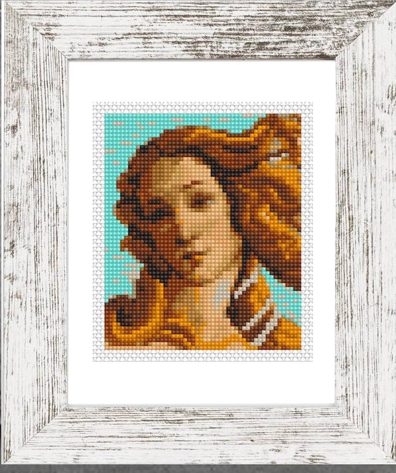 May include: Framed cross-stitch art featuring a portrait of a woman with long, flowing auburn hair. The artwork is set against a light blue background and framed in a distressed white wooden frame. The image is a close-up of the face.
