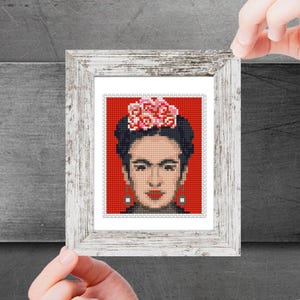 May include: A framed print of a portrait of Frida Kahlo with a flower crown and earrings. The background is red.