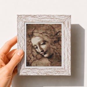 Puede incluir: Un patrón de punto de cruz enmarcado con una imagen en tonos sepia de una escultura clásica. El marco blanco tiene un acabado envejecido. El texto "Mini Art Cross Stitch Pattern PDF" está en la parte inferior.