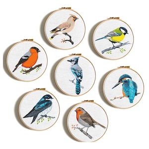 Może przedstawiać: Zestaw siedmiu obręczy do haftu z różnymi wzorami ptaków. Ptaki są wyszywane w różnych kolorach, w tym niebieskim, czerwonym, żółtym i zielonym. Każda obręcz jest wykonana z drewna i ma białe tło z tkaniny.