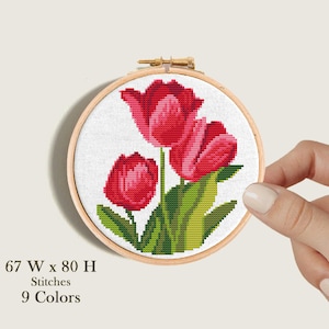 May include: A cross-stitch pattern of three red tulips with green leaves in a wooden embroidery hoop. The pattern is 67 stitches wide and 80 stitches high and uses 9 colors.