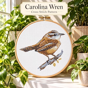 May include: A circular wooden embroidery hoop containing a cross stitch pattern of a Carolina Wren bird perched on a branch. The text Carolina Wren Cross Stitch Pattern is displayed in a rectangular label above the hoop on a white background.
