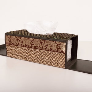 May include: A brown and green tissue box cover with a woven pattern and an elephant design. The cover is open and the tissue box is visible inside.