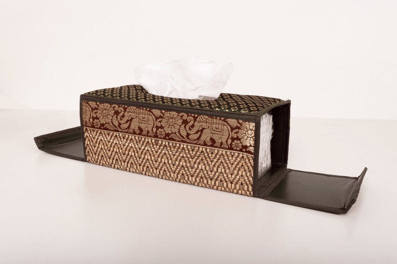 May include: A brown and green tissue box cover with a woven pattern and an elephant design. The cover is open and the tissue box is visible inside.