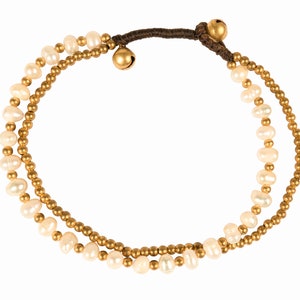May include: A double-strand bracelet with white pearls and gold beads. The bracelet has a brown cord with a gold bell charm.