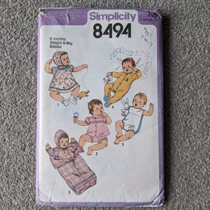 Może przedstawiać: Vintage wzór Simplicity 8494 dla niemowląt, z ilustracjami niemowląt w różnych strojach. Okładka wzoru jest fioletowa z napisem "Simplicity 8494" i szczegółami dla niemowląt w wieku 6 miesięcy o wadze 6-8 kg.
