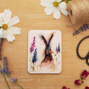 May include: A watercolor painting of a brown hare with long ears, looking directly at the viewer. The hare is surrounded by purple and blue wildflowers.