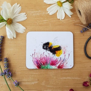 Puede incluir: Una pintura de acuarela de un abejorro en una flor rosa. La abeja es amarilla y negra con un cuerpo peludo. La flor tiene un centro verde y pétalos rosados.