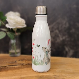 May include: White stainless steel water bottle with a colorful illustration of a hare looking at a bee in a field of flowers.