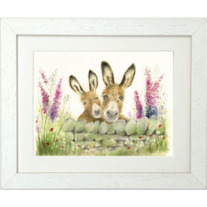 May include: Two brown donkeys peek over a stone wall with green grass and pink flowers in front of them. The donkeys have brown fur and large ears. The donkey on the right is looking directly at the viewer.