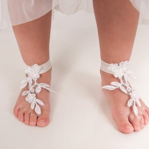Puede incluir: Sandalias descalzas de encaje blanco con una tira de tobillo de cinta. Las sandalias est&aacute;n hechas de encaje blanco delicado y presentan un dise&ntilde;o floral.