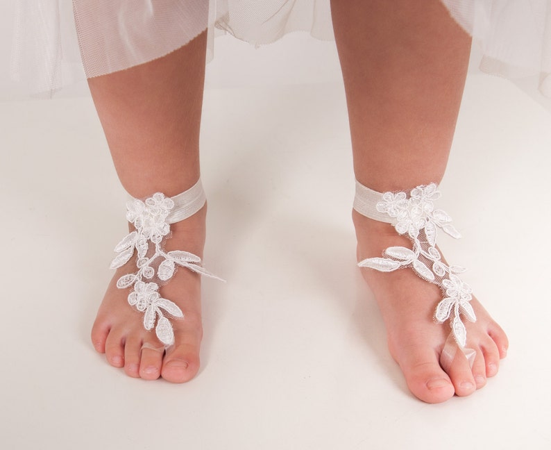 Puede incluir: Sandalias descalzas de encaje blanco con una tira de tobillo de cinta. Las sandalias est&aacute;n hechas de encaje blanco delicado y presentan un dise&ntilde;o floral.