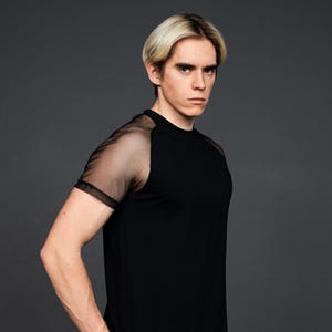 Puede incluir: Una camiseta negra de manga corta con un panel de malla en la parte superior del brazo. La camiseta tiene cuello redondo y un ajuste holgado.
